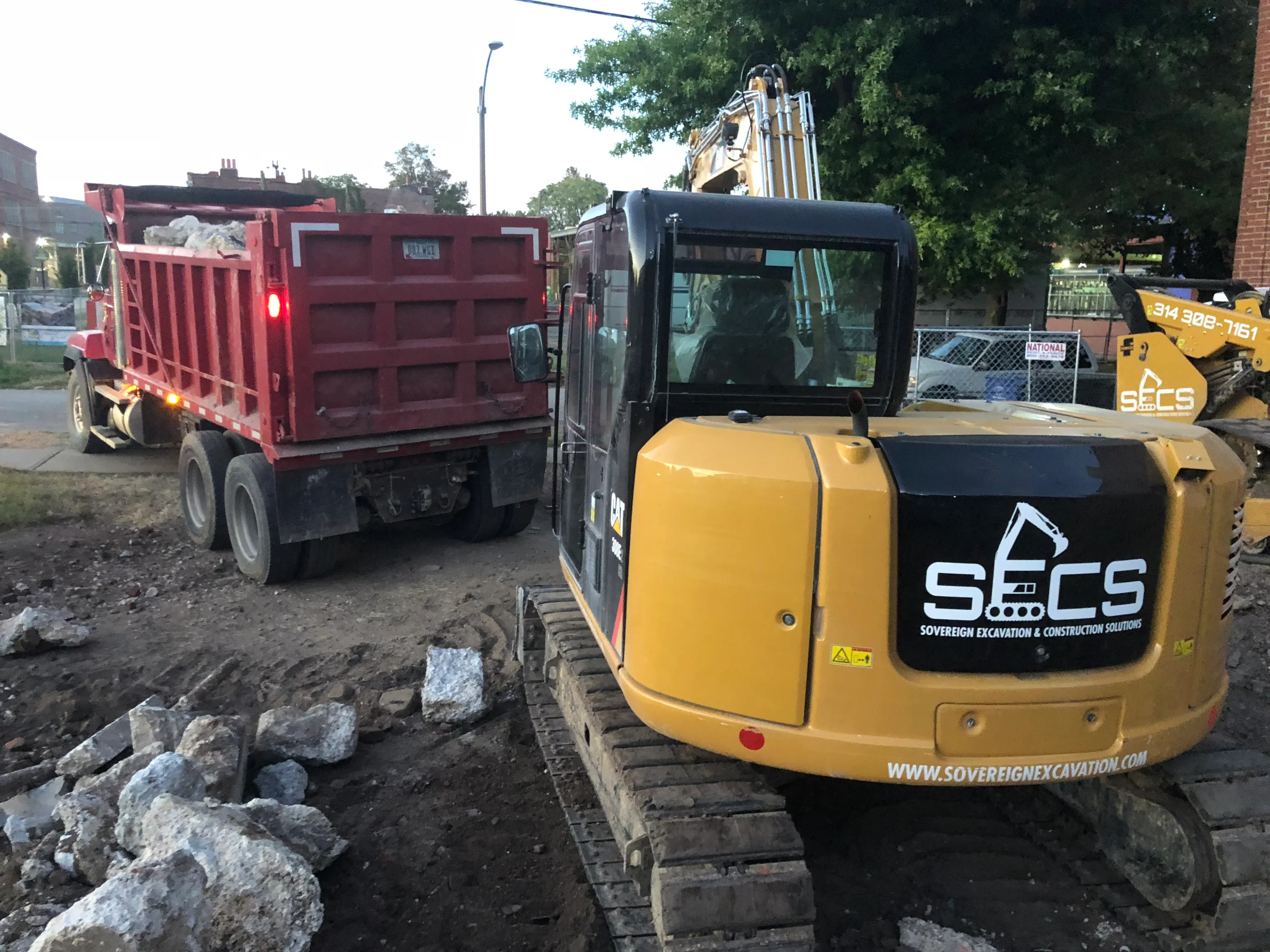 Compact excavator and dump truck removing concrete and masonry debris from demolition site