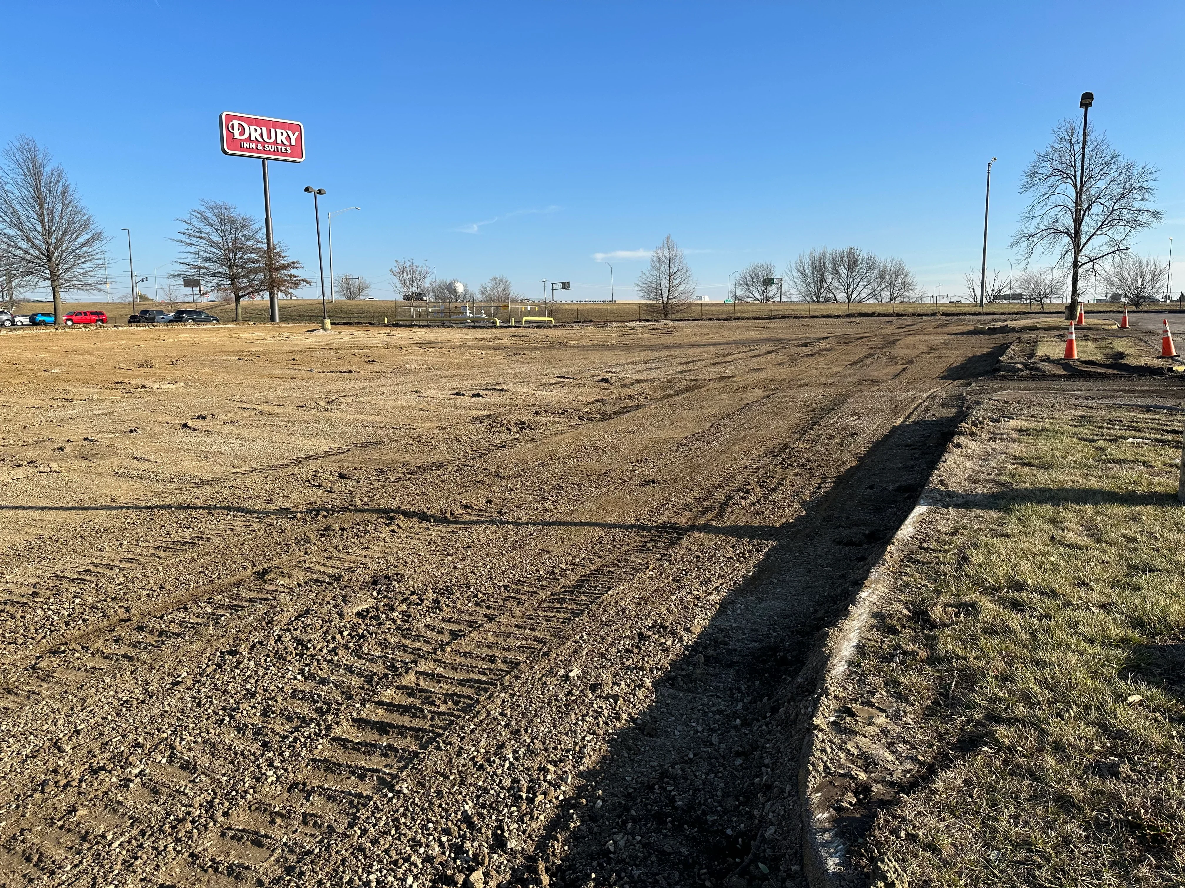 Excavated commercial lot with graded soil, drainage swale, and traffic cones