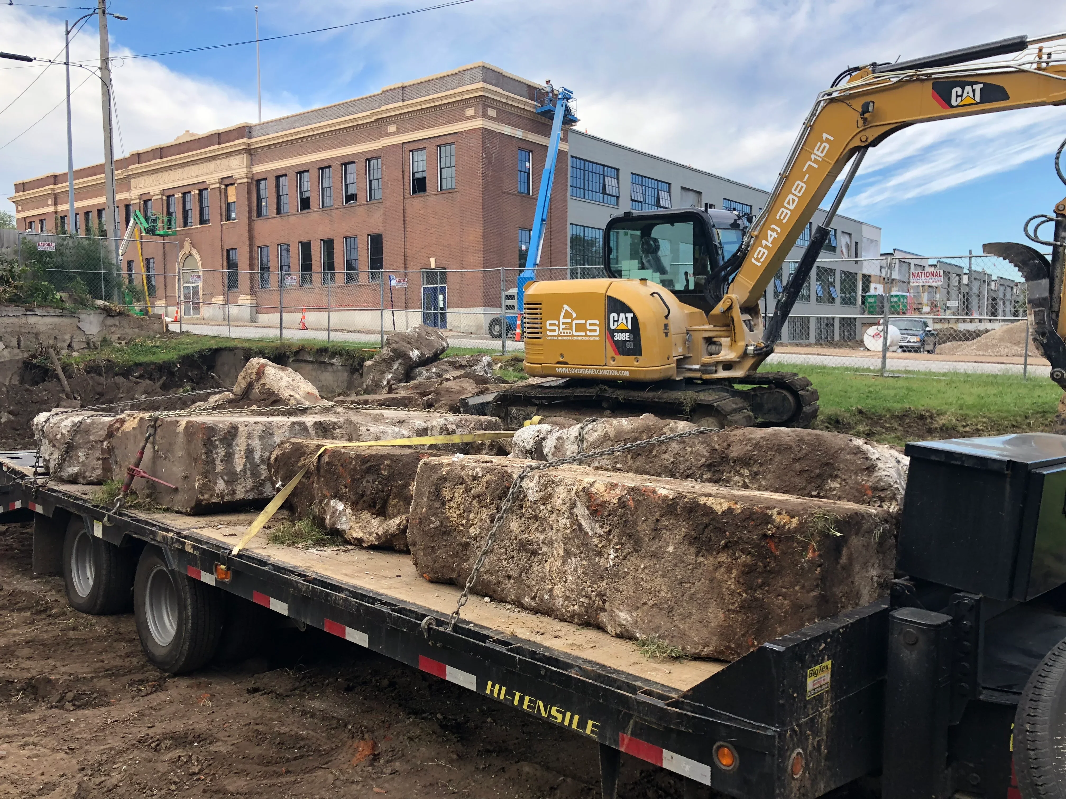 CAT excavator loading large concrete foundation chunks onto flatbed truck during demolition