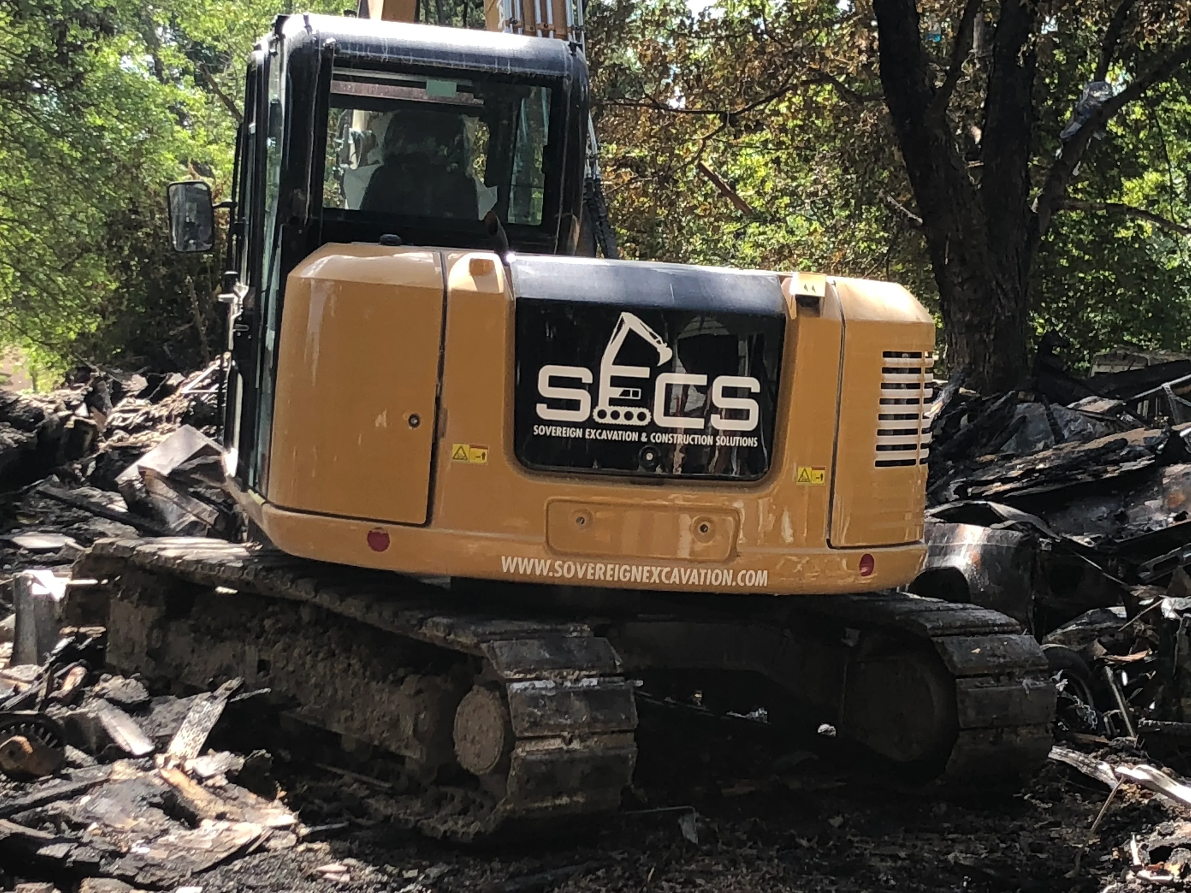 Yellow tracked excavator on wooded demolition site with felled logs and debris